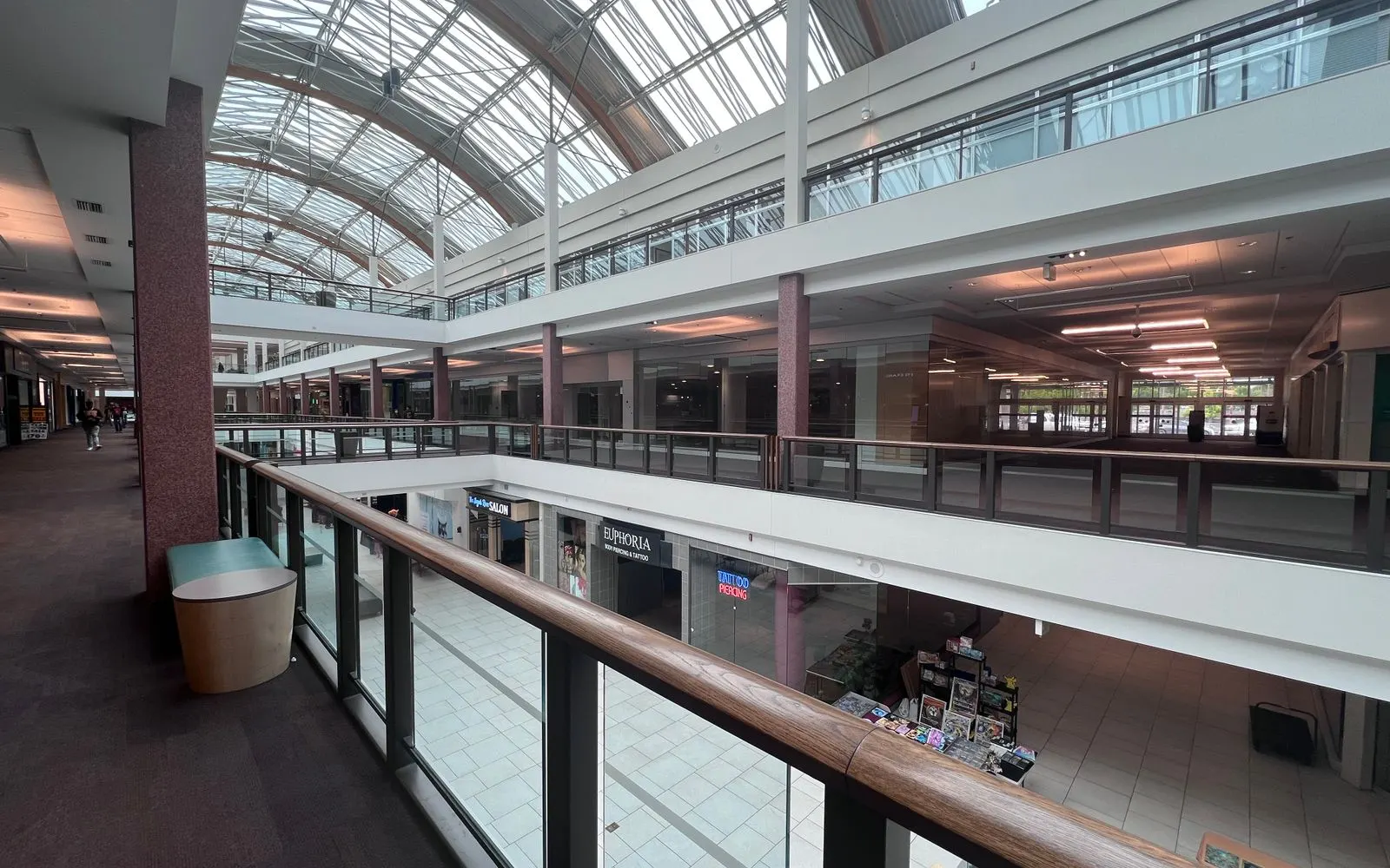 The upper walkways of a multi-level shopping mall under an arched glass roof