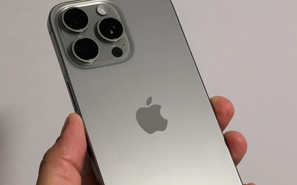 A hand holding a silver smartphone, its rear cameras in focus