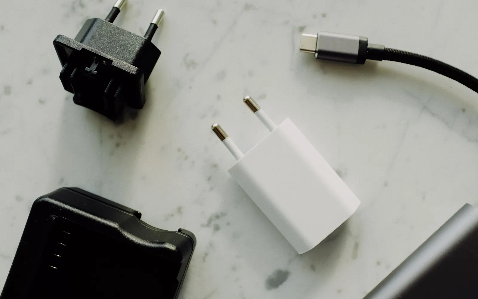 A braided USB-C cable beside a white wall charger and plug adapters on a marble surface