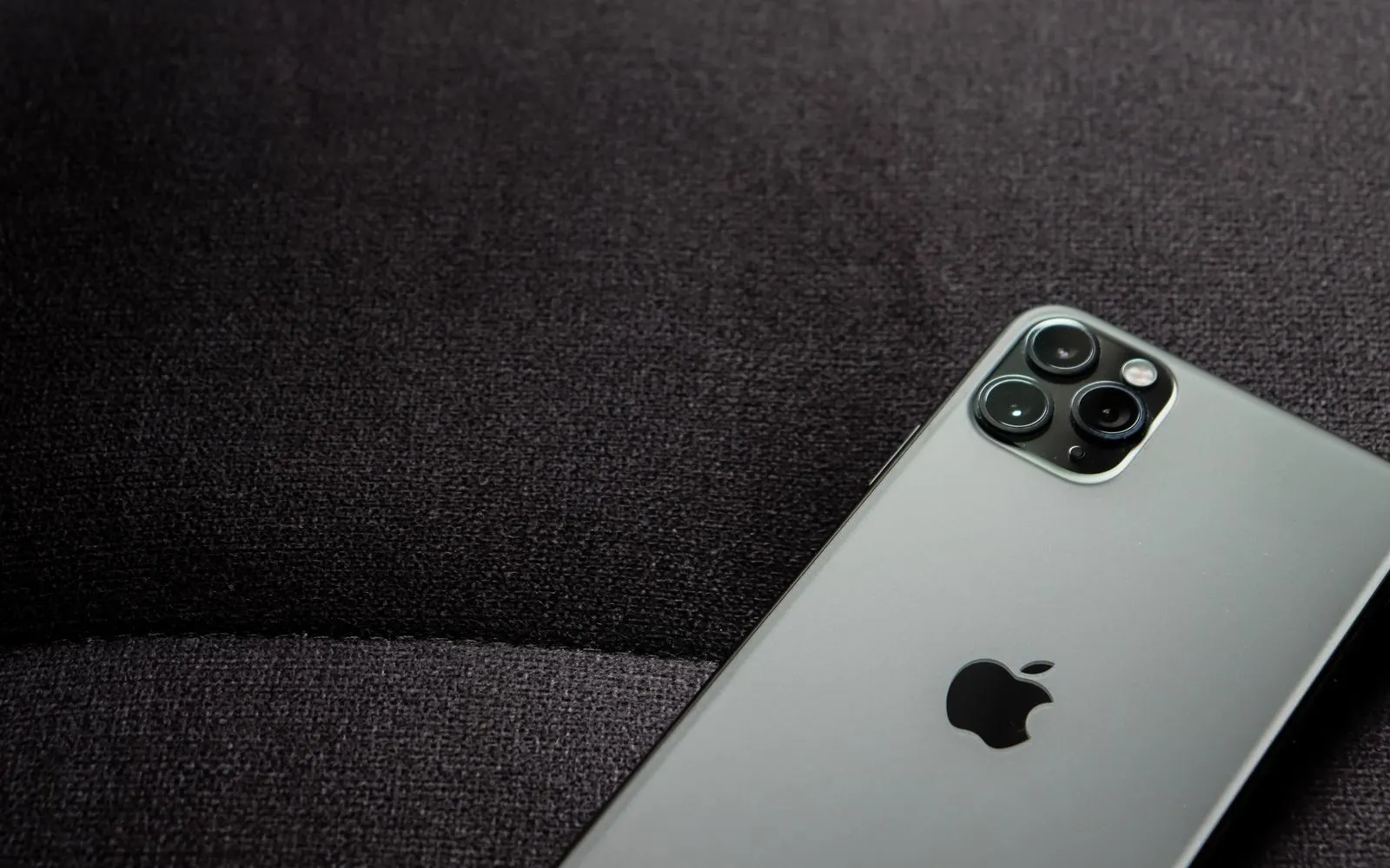 An iPhone Pro lying face down on dark fabric, its triple camera visible