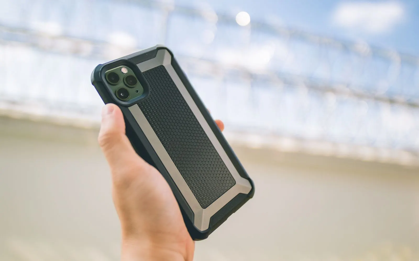 A hand holding an iPhone in a rugged protective case with raised edges