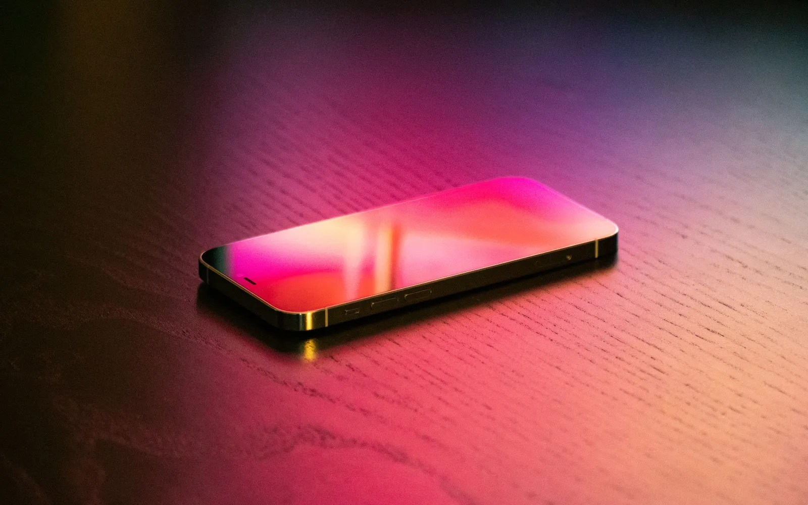 An iPhone lying screen up on a wooden table, its display glowing pink and orange