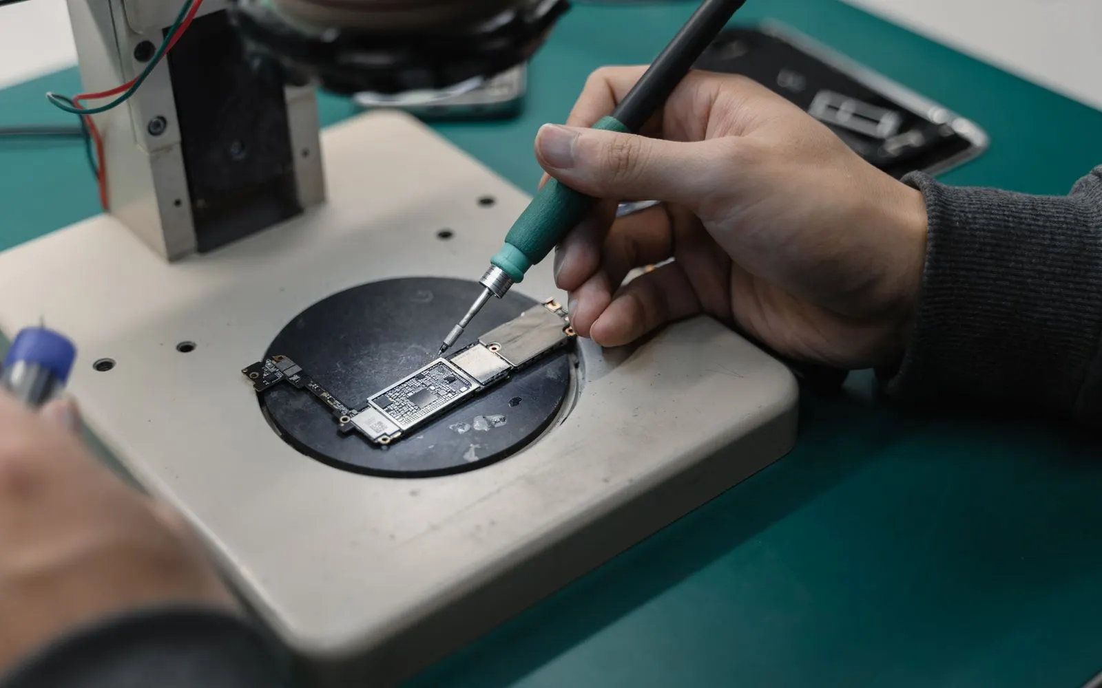 A technician working on an iPhone logic board held in a repair fixture
