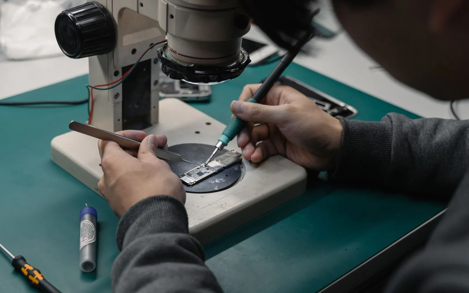A technician working on a phone circuit board under a microscope at a repair bench