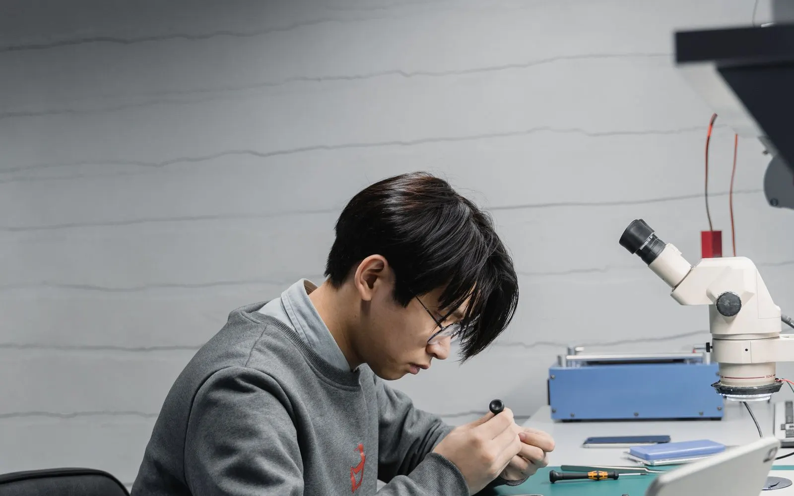 A technician working on a phone at a repair bench beside a microscope