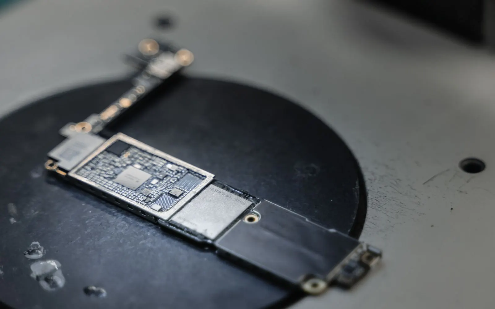 An iPhone logic board laid on a repair bench mat