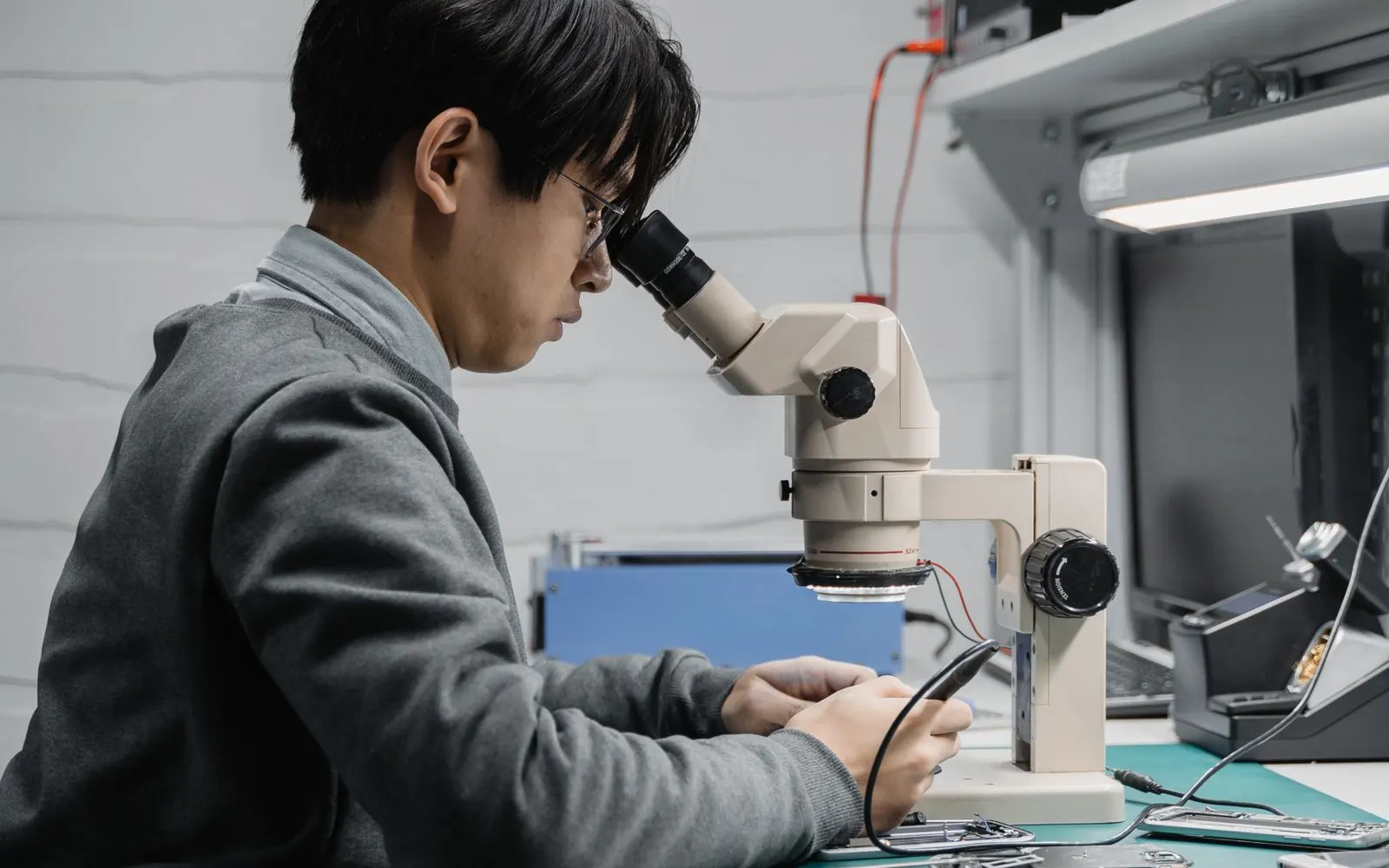 A technician seated at a microscope on a repair bench