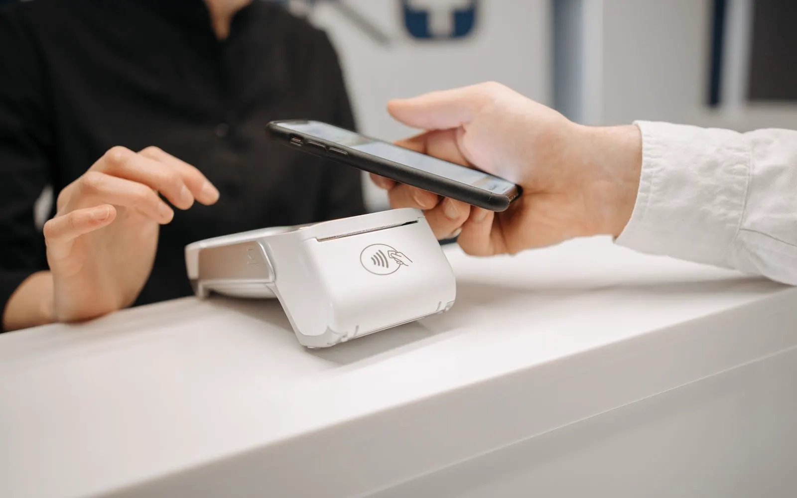 A customer paying at a shop counter with a phone in hand