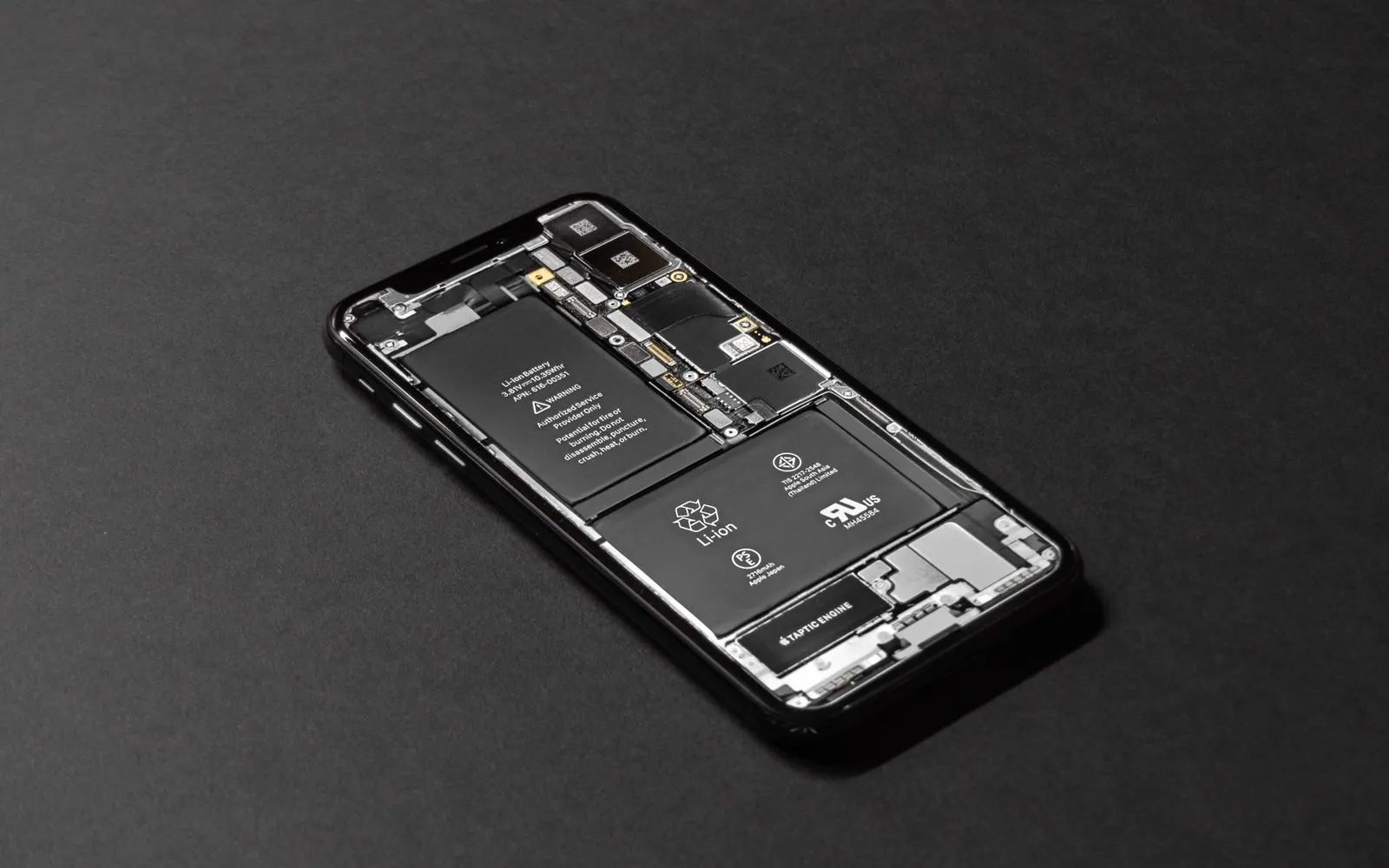 A smartphone opened up on a dark surface with its internal components visible