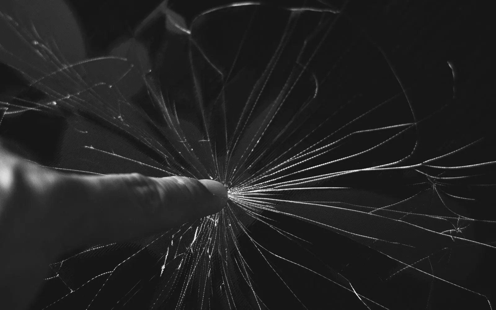 A fingertip resting on shattered phone glass, cracks spreading out from the point of impact