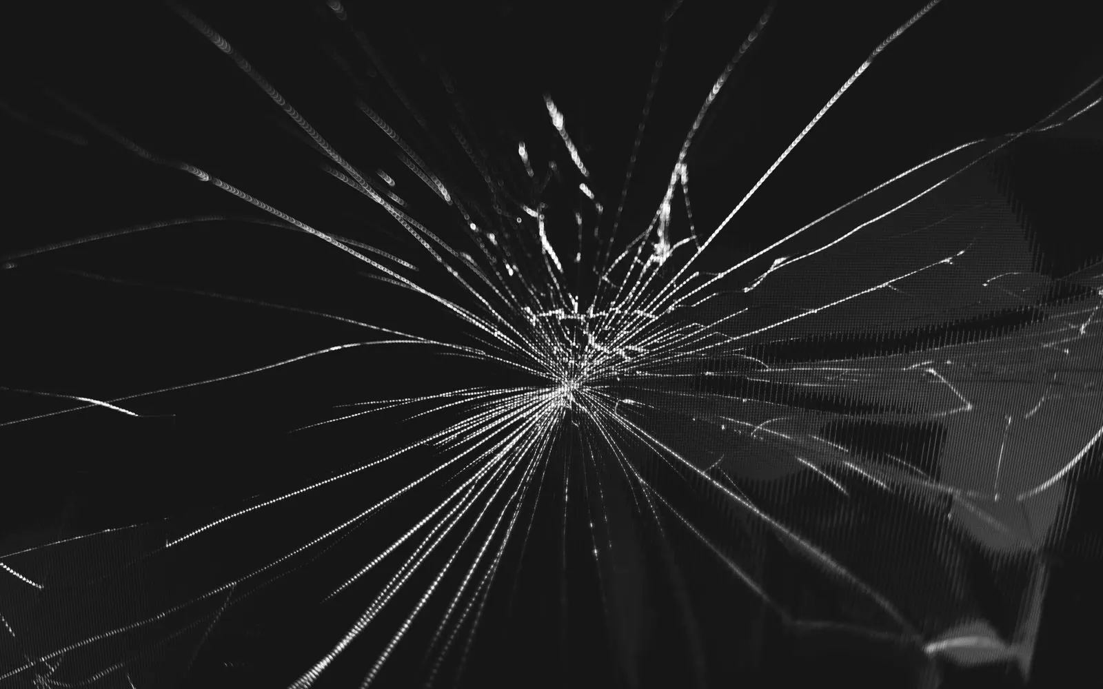 Cracks spreading out from a single impact point across black screen glass