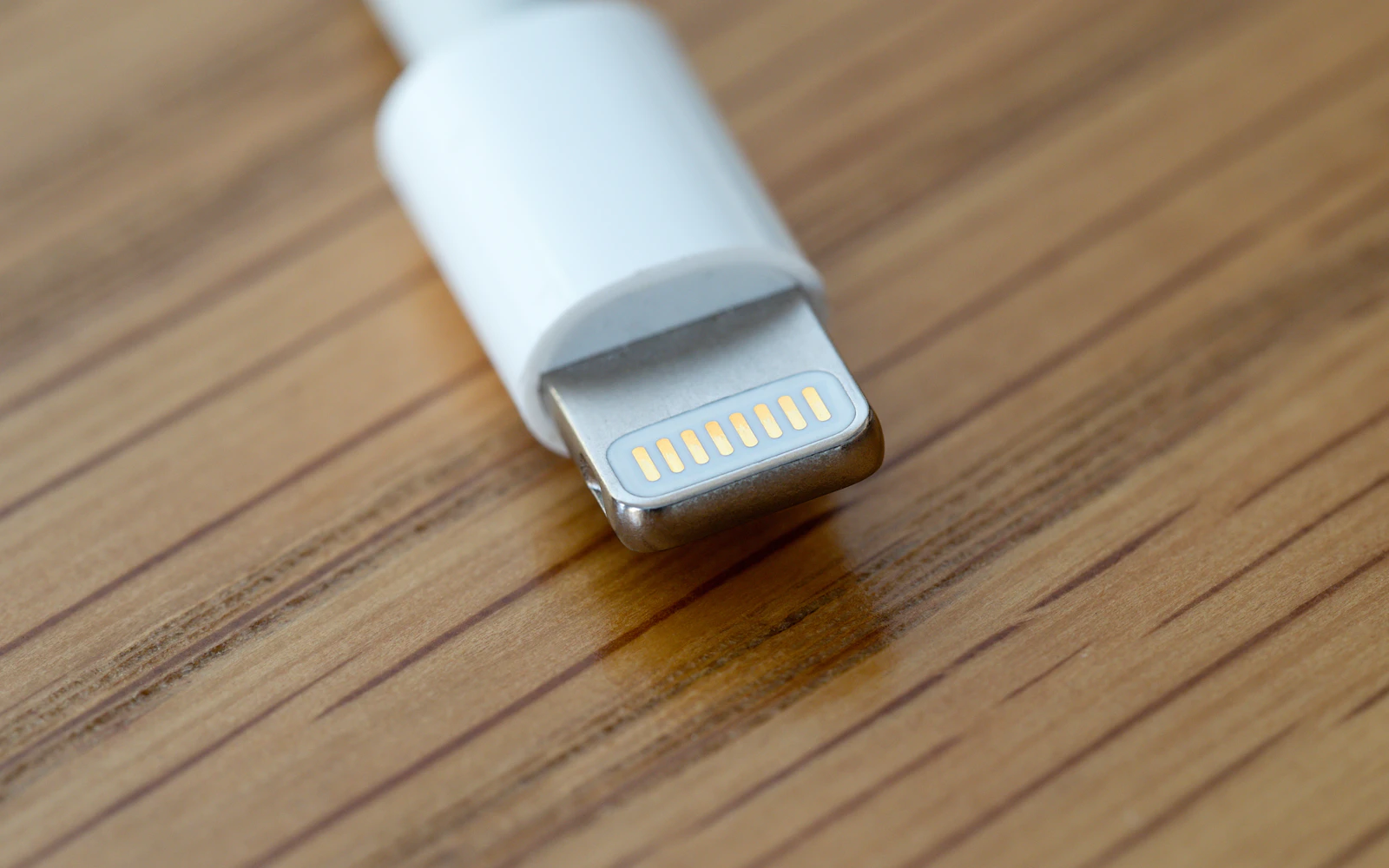 The gold contacts of a white Lightning charging plug resting on a wooden table