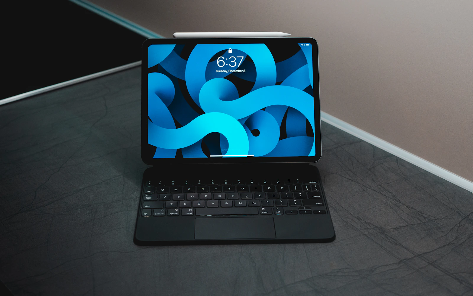 An iPad on a black Magic Keyboard, its lock screen showing the time, on a dark desk