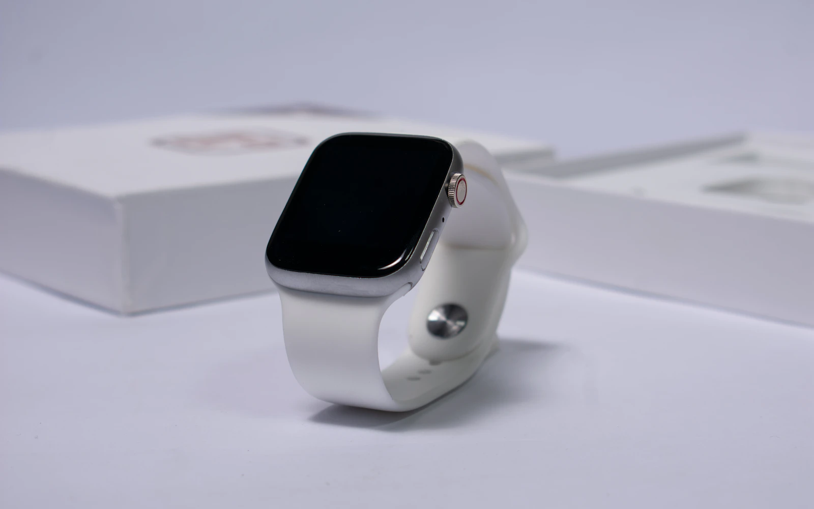A silver Apple Watch with a white sport band standing beside its box