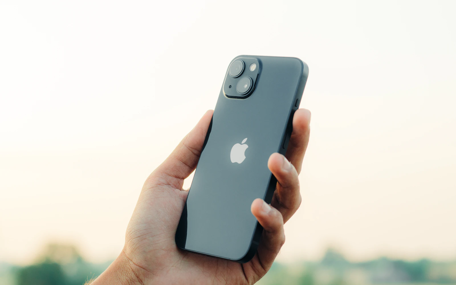 A hand holding up a dark iPhone with its back glass and dual rear cameras facing the viewer