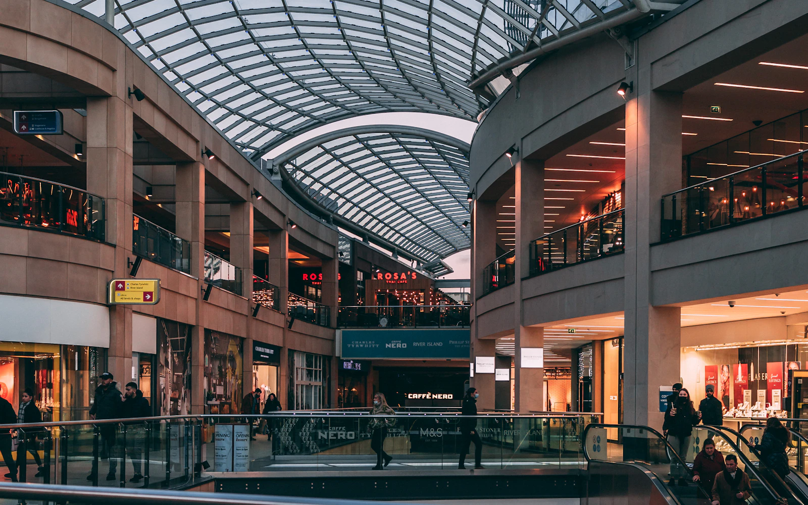 Shoppers on two levels of a shopping mall under a curved glass roof
