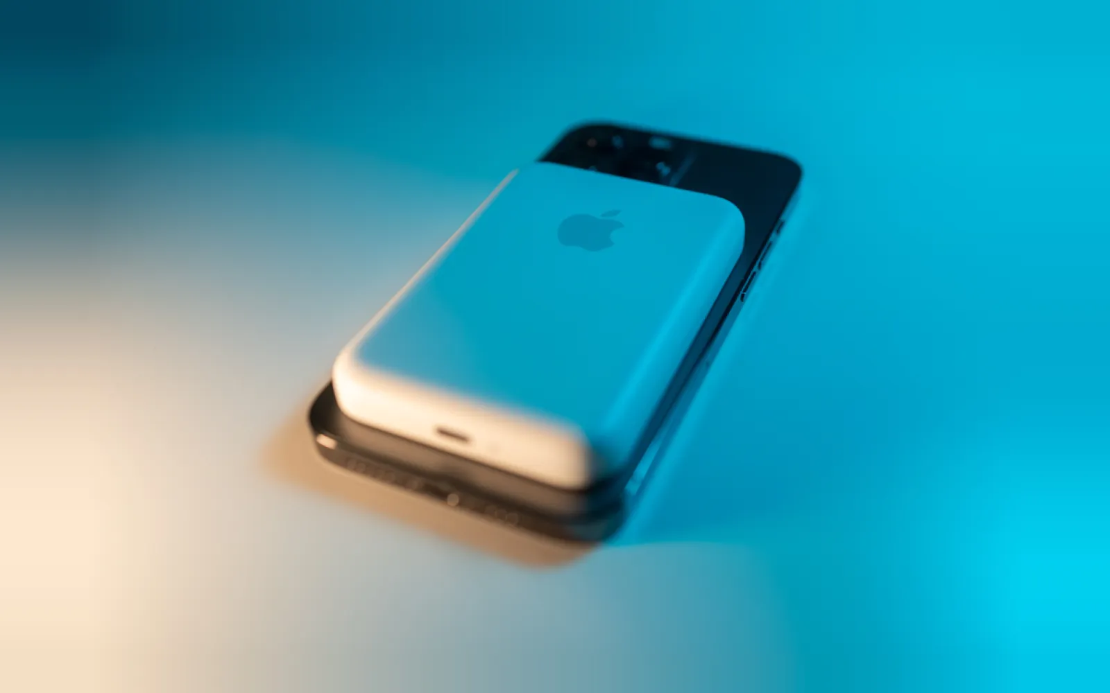 An iPhone Pro with a white MagSafe battery pack attached to its back, on a blue and cream backdrop