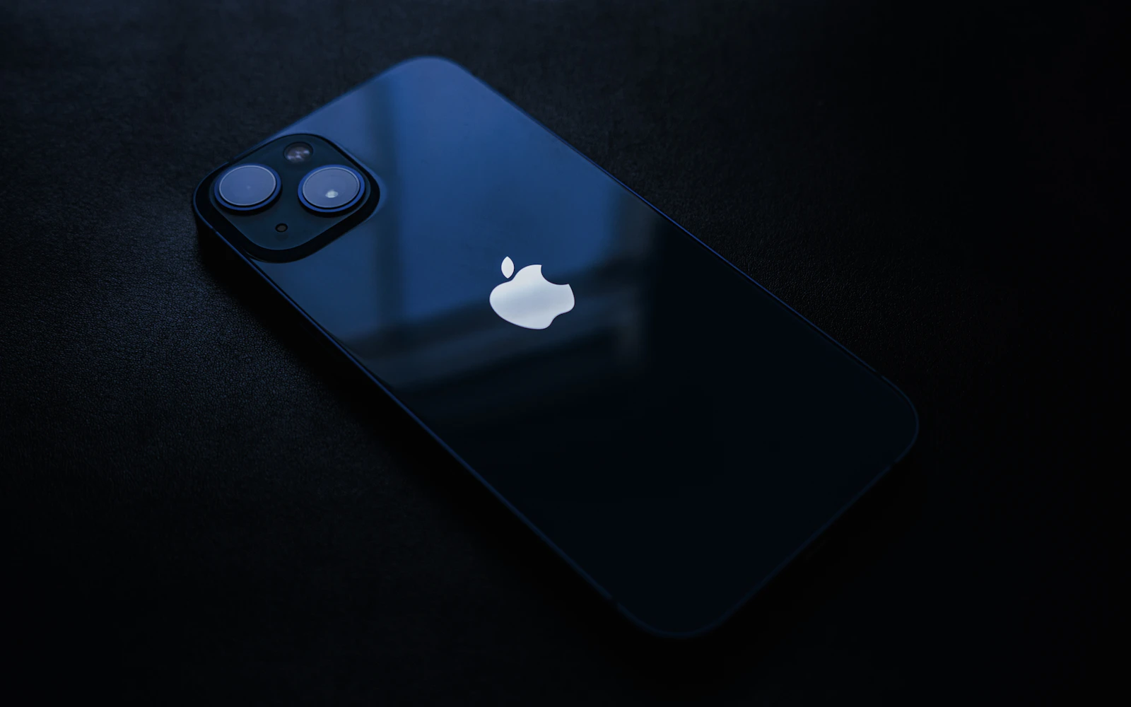 A dark blue iPhone lying face down on a black surface, its dual rear cameras catching the light