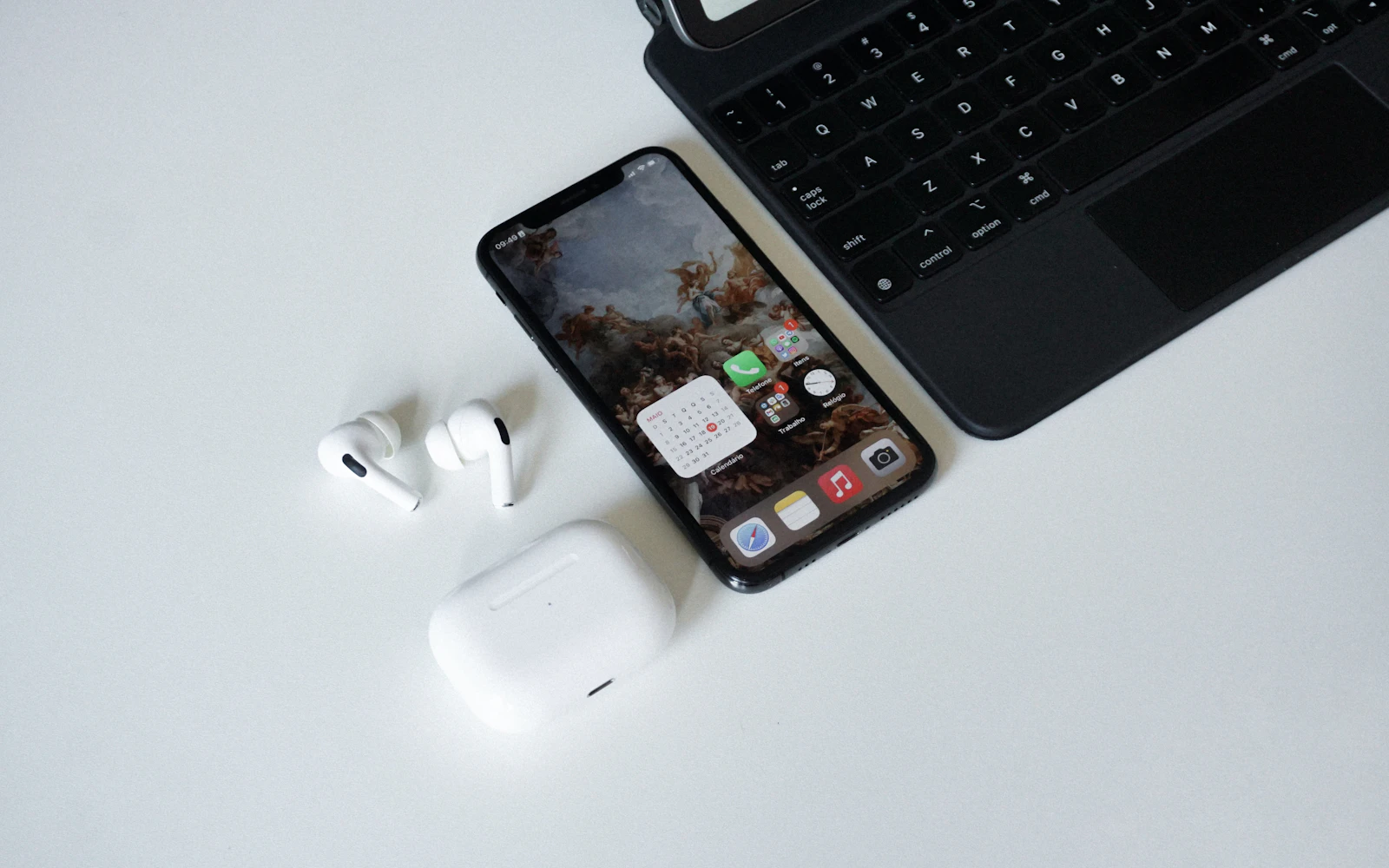 An iPhone beside a pair of wireless earbuds and their open case on a white desk