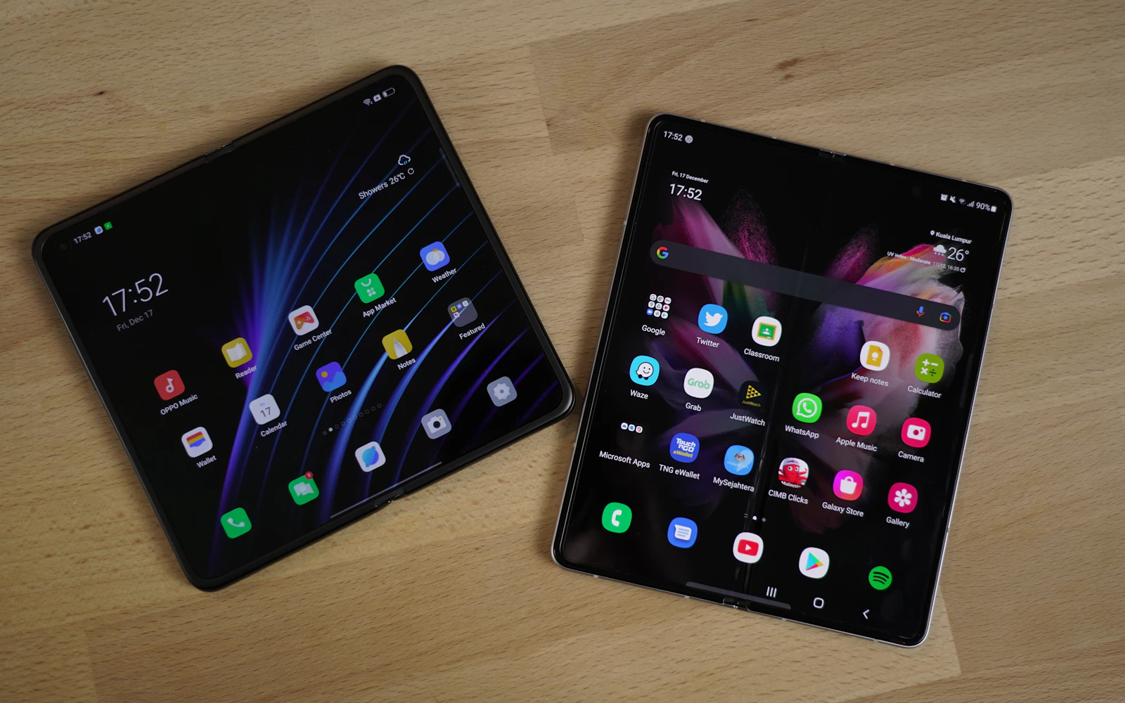 Two unfolded Samsung Galaxy Z Fold phones lying on a wooden table, both showing their home screens
