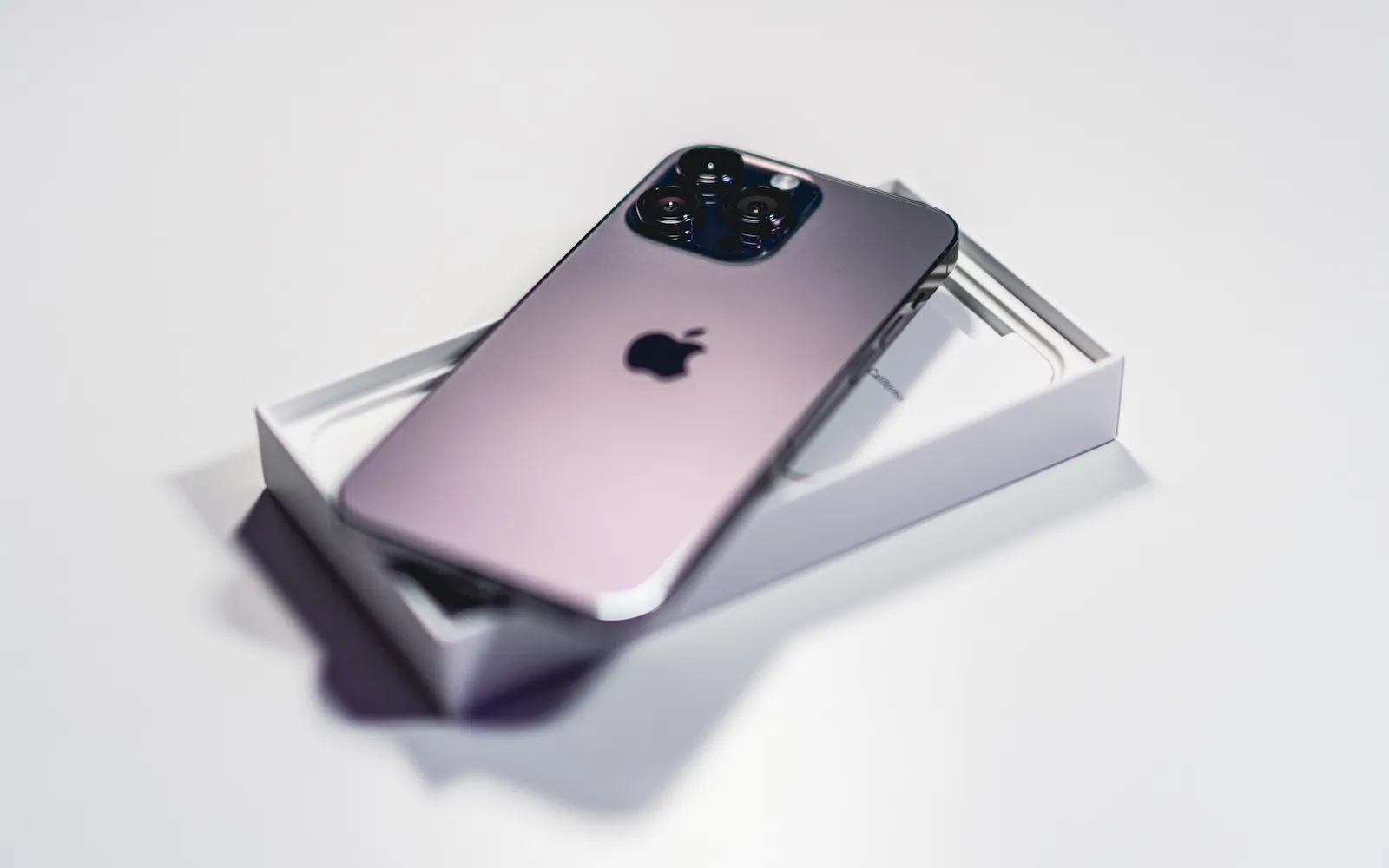 A purple iPhone Pro resting on its open box, its triple rear camera facing up