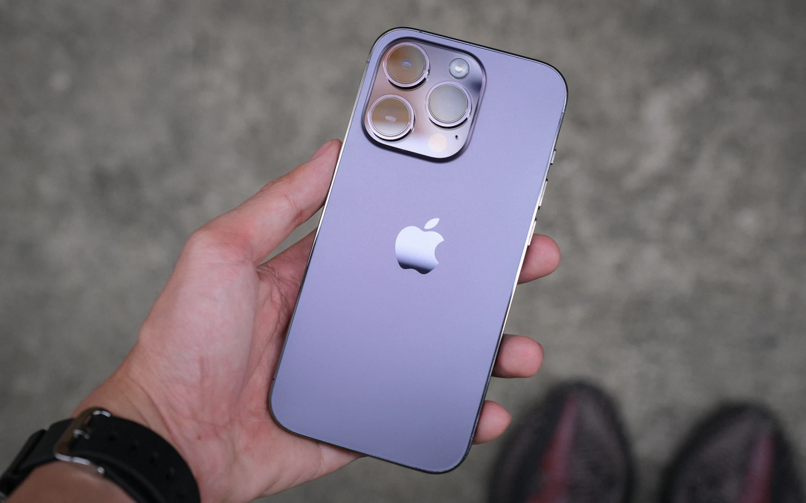 A hand holding a purple iPhone Pro with its back and triple camera facing the viewer