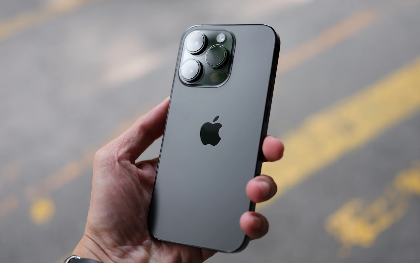 A hand holding a graphite iPhone Pro with its back and triple camera facing the viewer