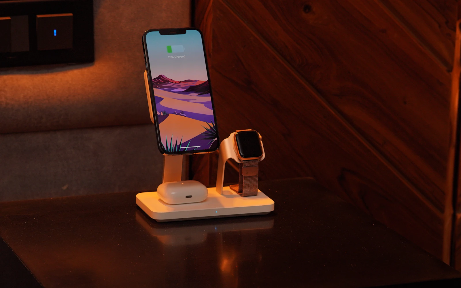 An iPhone, an Apple Watch and an AirPods case charging together on a stand on a bedside table