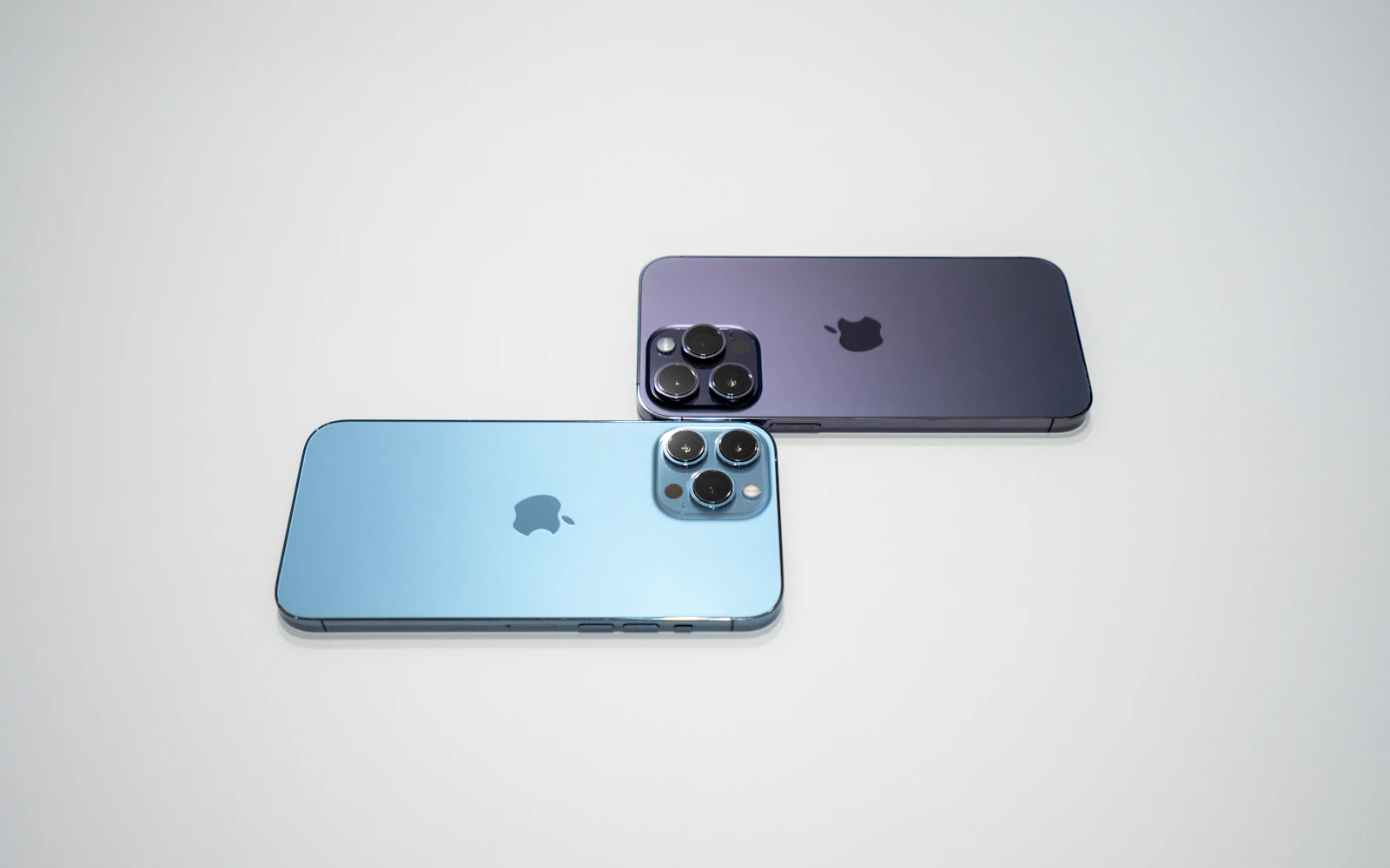 Two iPhone Pro models lying back up on a pale grey surface, their triple rear cameras in view