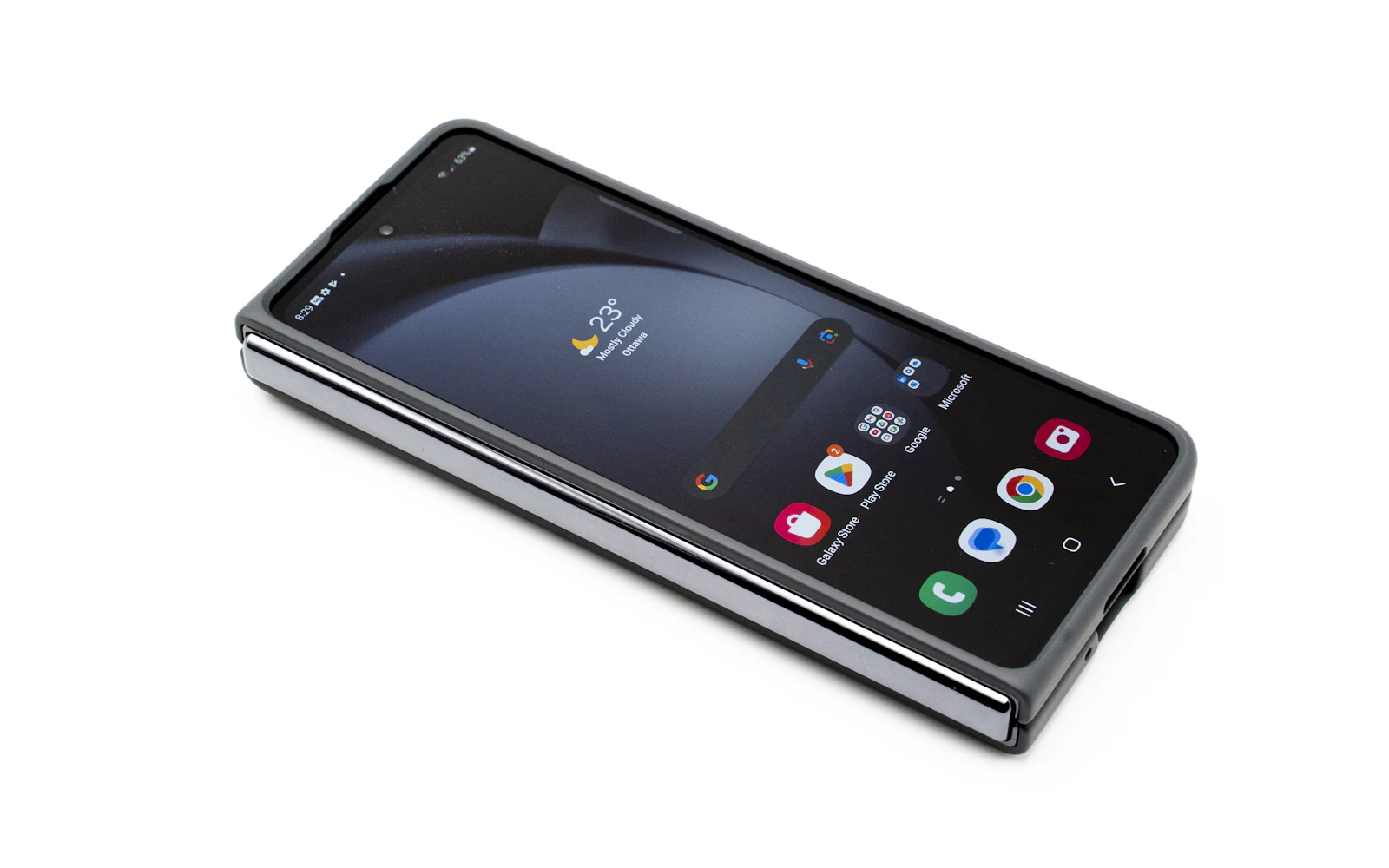 A folded Samsung Galaxy Z Fold lying on a white surface, its cover screen on and its USB-C port at the end