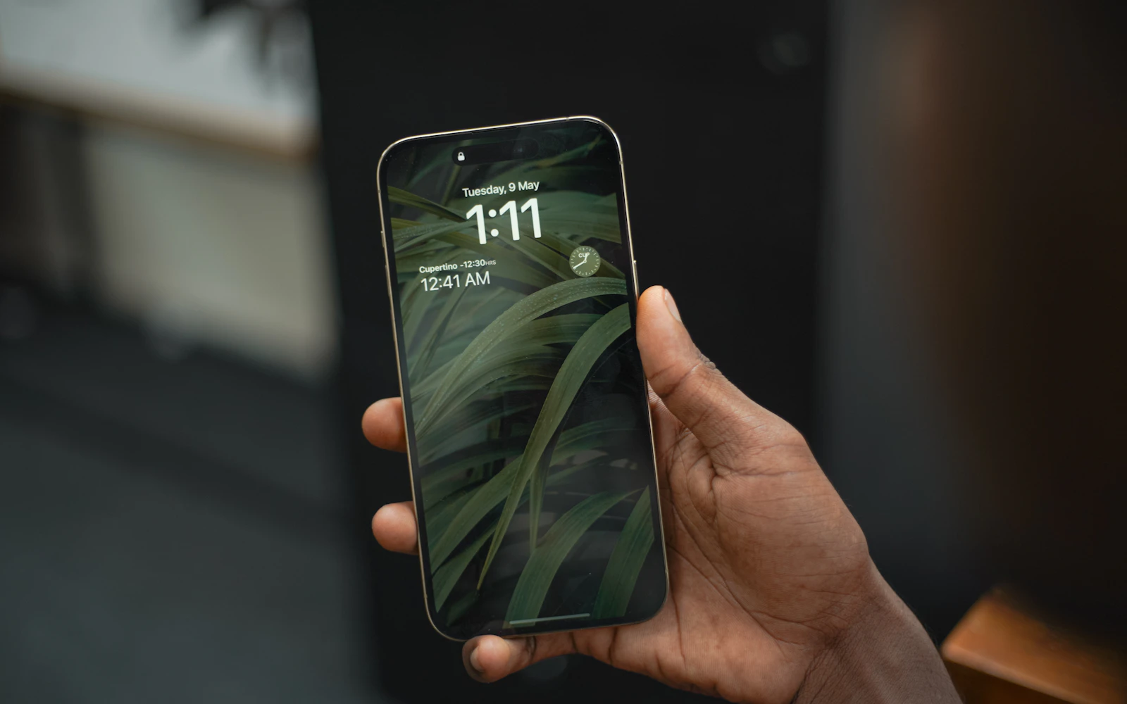 A hand holding an iPhone Pro showing the time on its lock screen