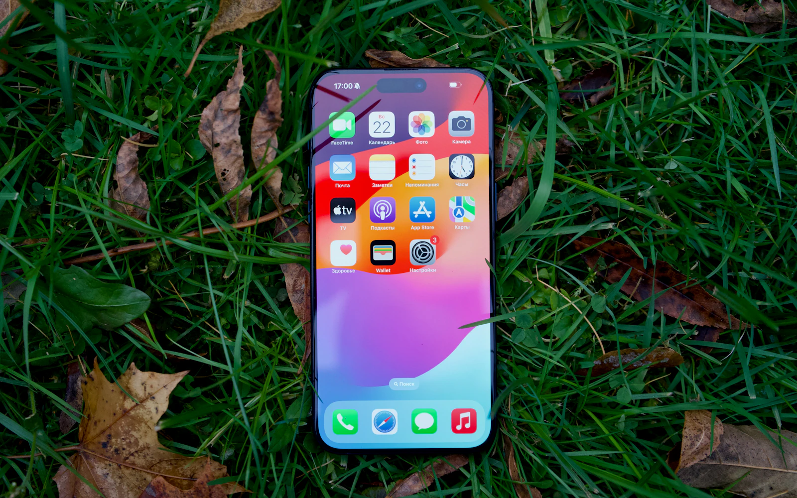 A recent iPhone lying face up on grass, its home screen lit