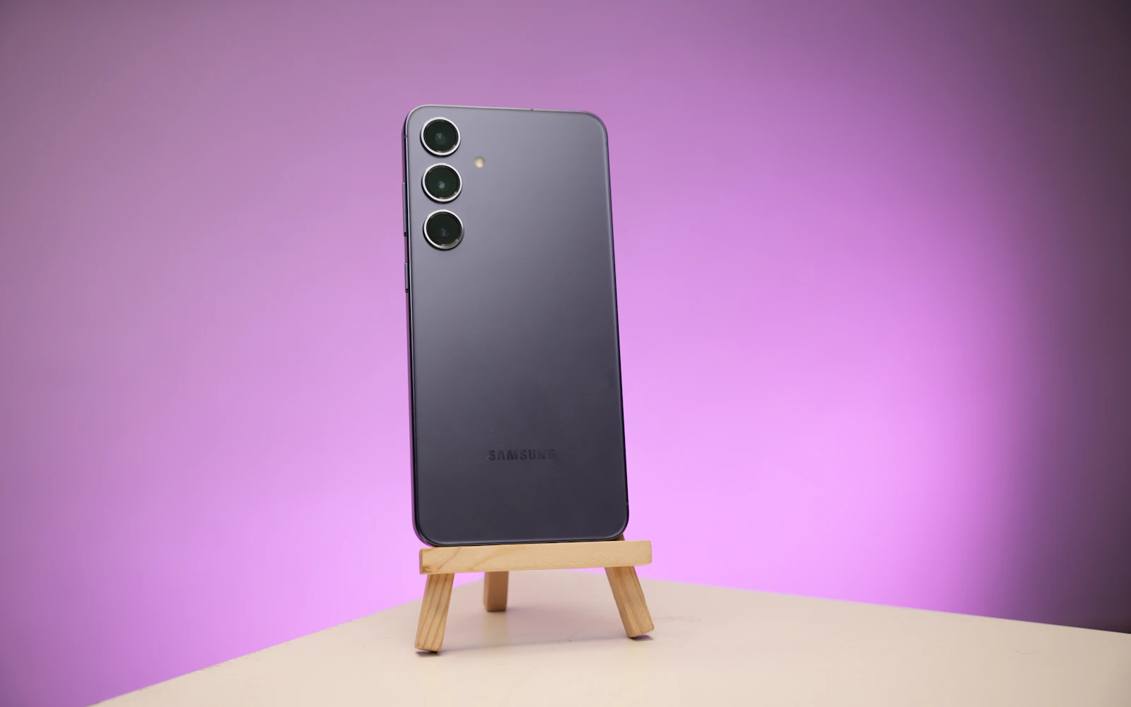 A Samsung Galaxy phone standing on a small wooden easel against a purple backdrop