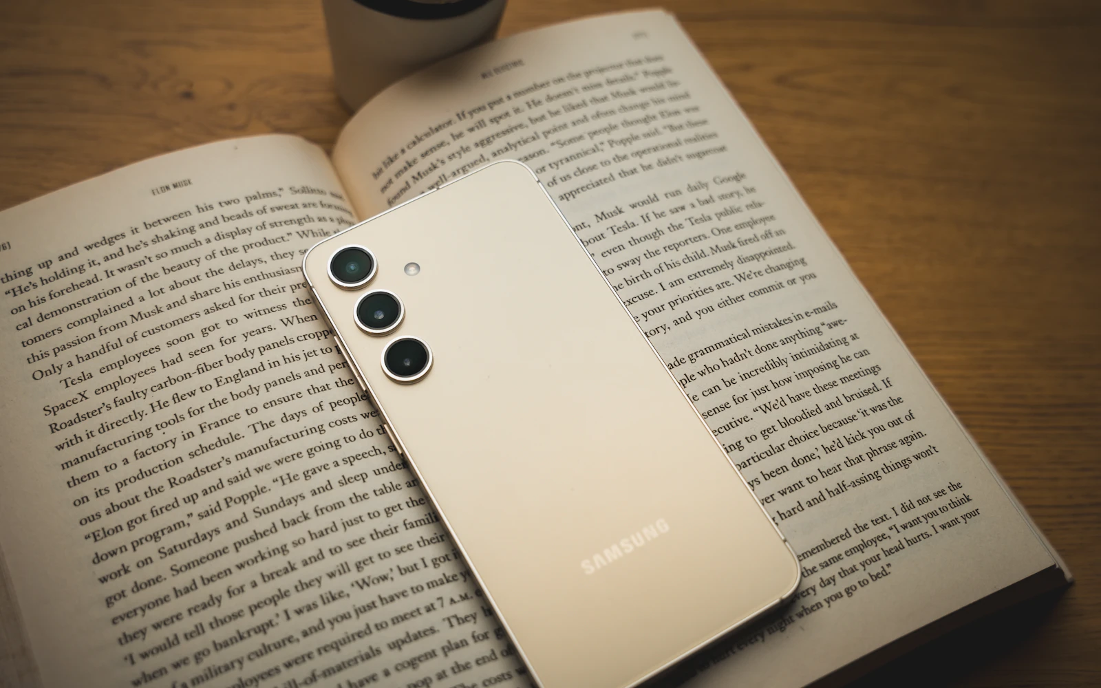 A cream Samsung Galaxy S24 lying face down on an open book, its three rear cameras in view