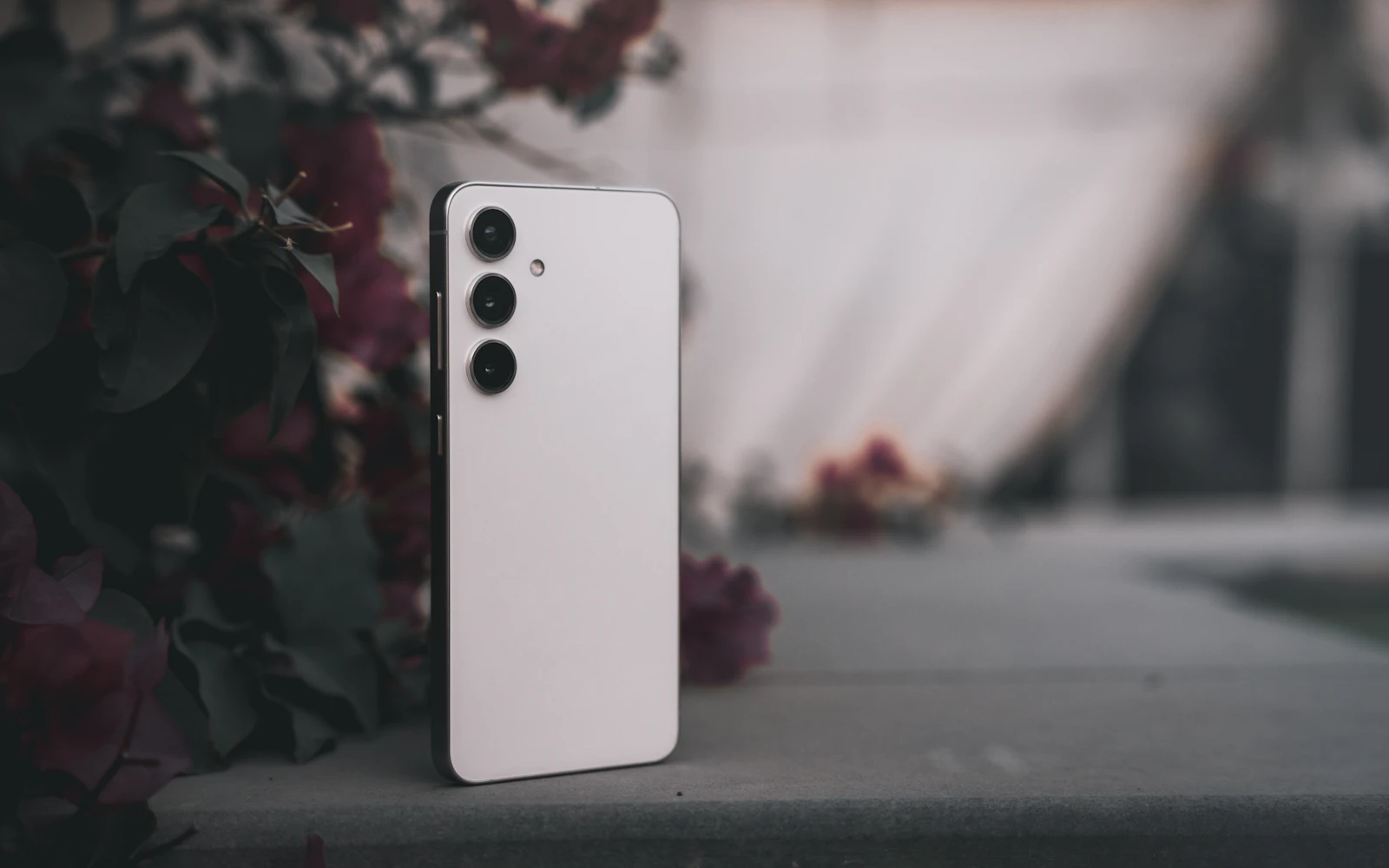 A white Samsung Galaxy standing upright on a stone ledge, its rear cameras facing out