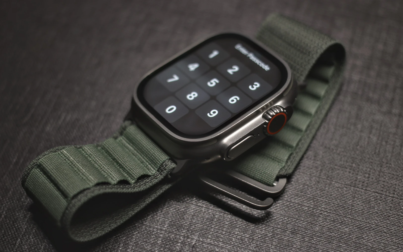 An Apple Watch Ultra with a green loop band lying on a dark textured surface