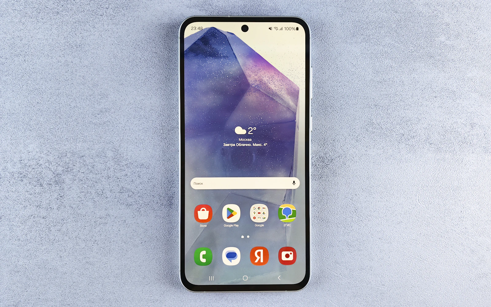 A Samsung Galaxy A series phone lying face up on a grey stone surface, its home screen on