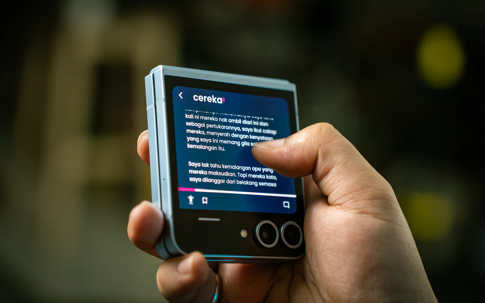 A hand holding a folded Samsung Galaxy Z Flip, a thumb scrolling text on its cover screen