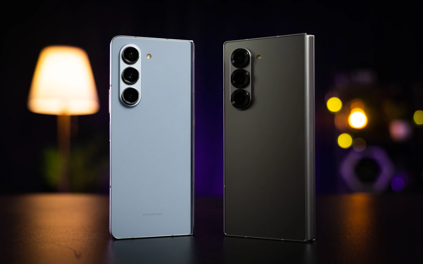 Two Samsung Galaxy Z Fold phones standing on a dark table, their triple rear cameras facing the lens