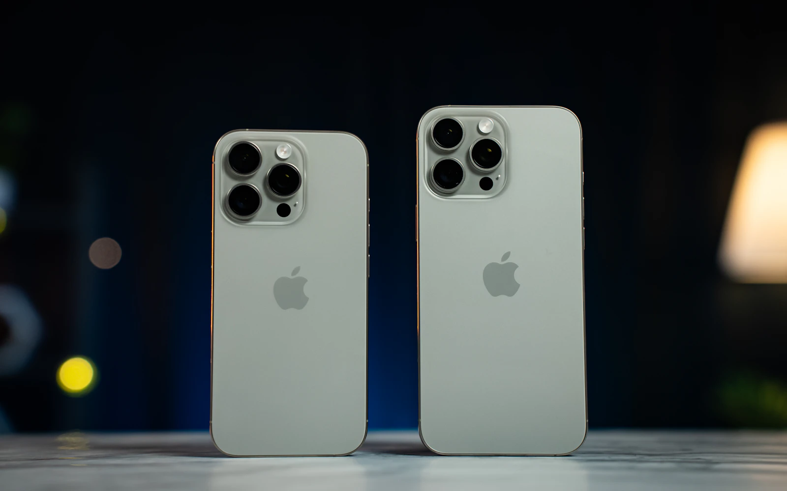 Two natural titanium iPhone Pro models standing side by side on a table, their backs facing out