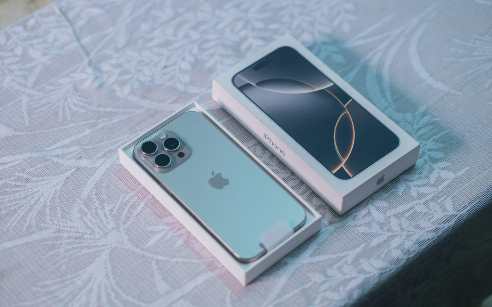 A new iPhone Pro lying in its open box on a patterned cloth