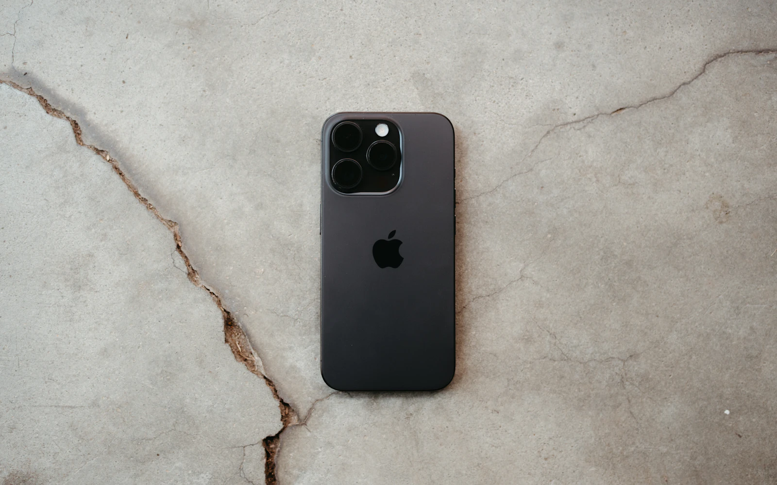 A dark iPhone Pro lying face down on a cracked concrete floor