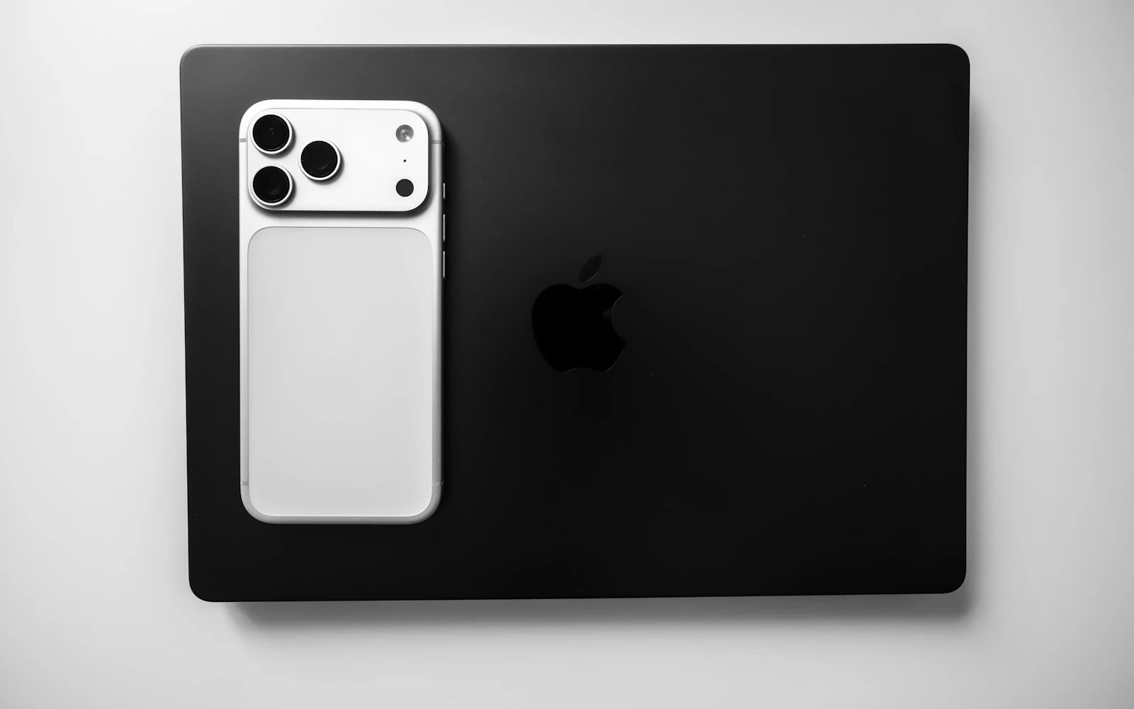 A white iPhone Pro lying on a black laptop, its rear cameras facing up