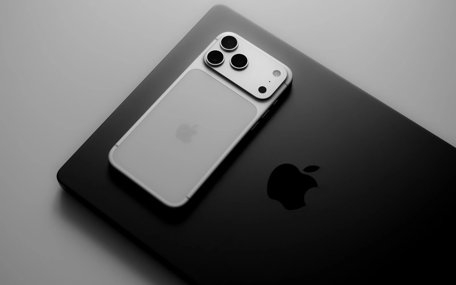 A white iPhone Pro lying on a black laptop under soft light, its camera plateau at the top