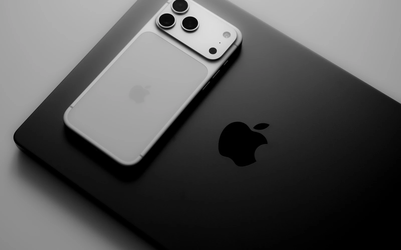 A silver iPhone Pro lying face down on a black laptop, its triple rear camera in view