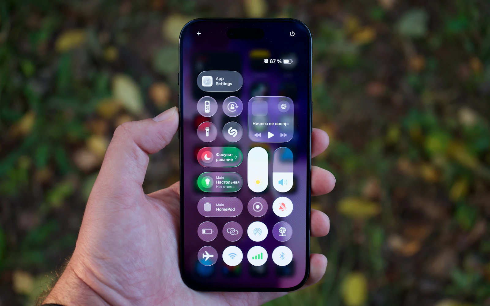 A hand holding a recent iPhone with Control Center open, the battery reading in the top corner
